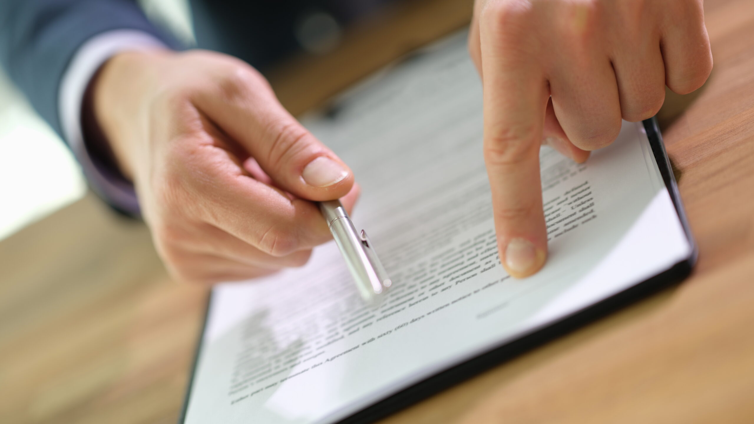 Two people reviewing a contract document together, one person holding a pen while the other points to a specific section of the text on the paper