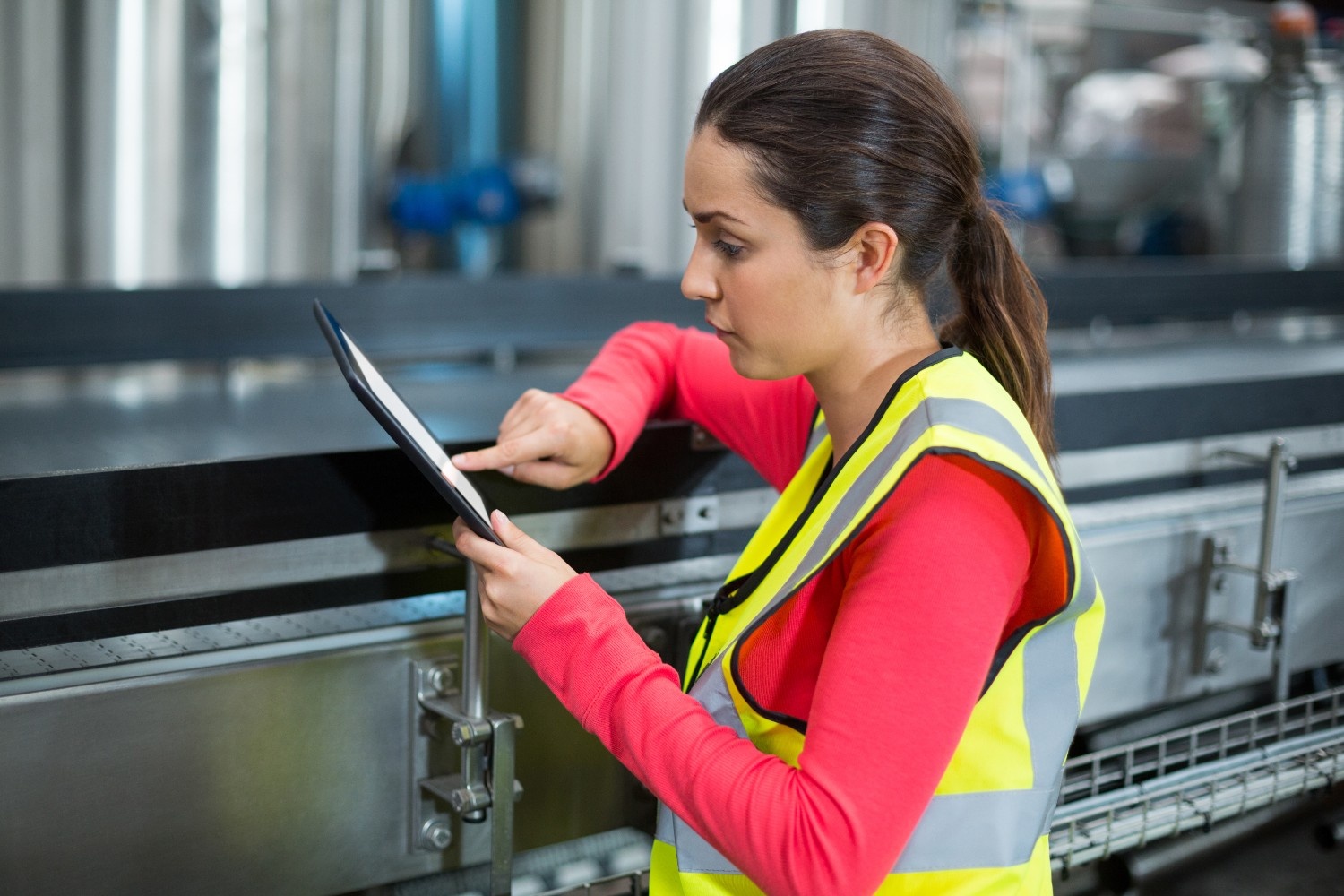 Female industrial worker in a safety vest reviewing data on a tablet, representing eSignature for Manufacturing in a factory setting.