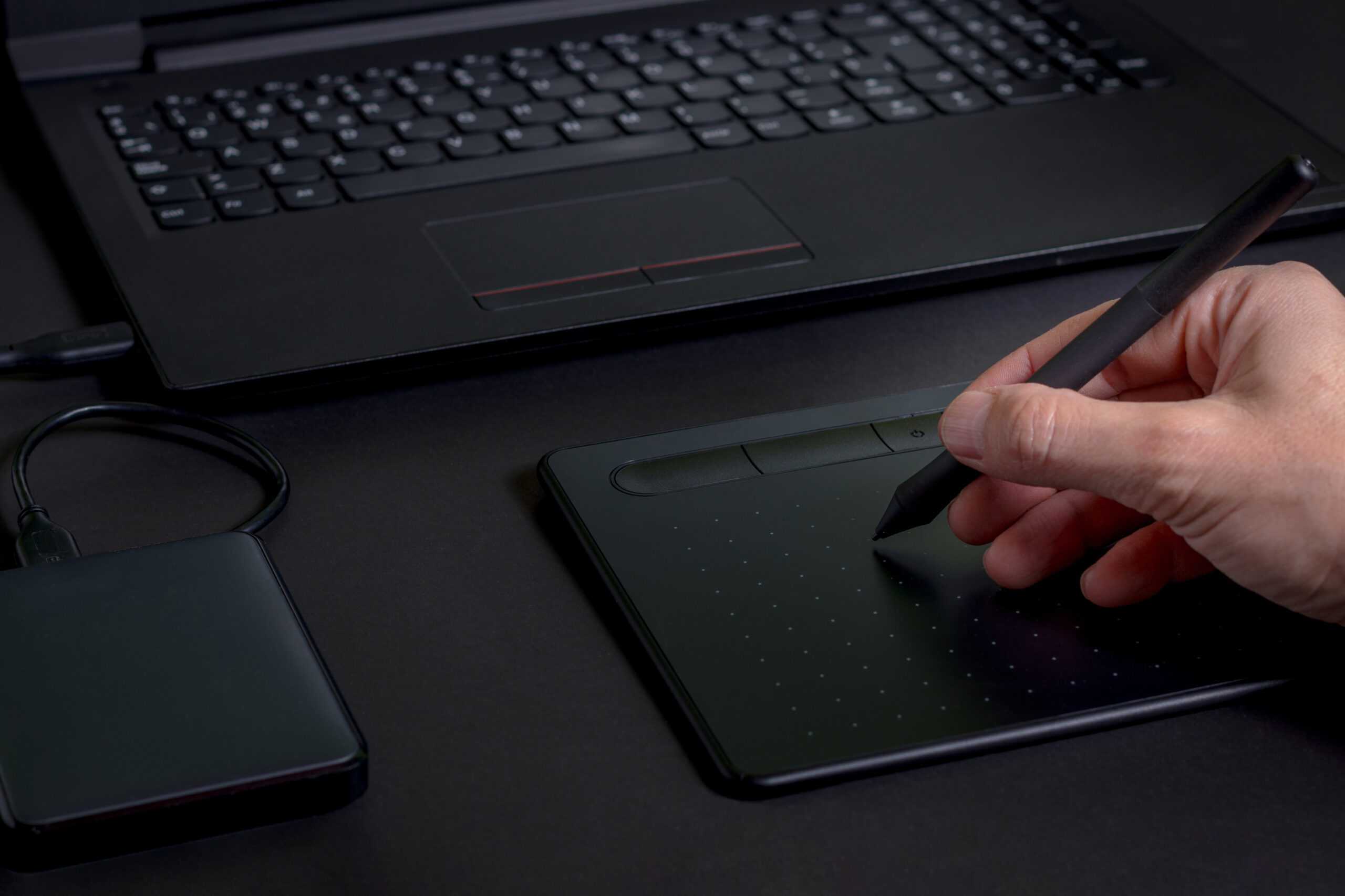 Person using a digital pen tablet to create a free electronic signature, demonstrating an efficient electronic mobile sign setup connected to a laptop.