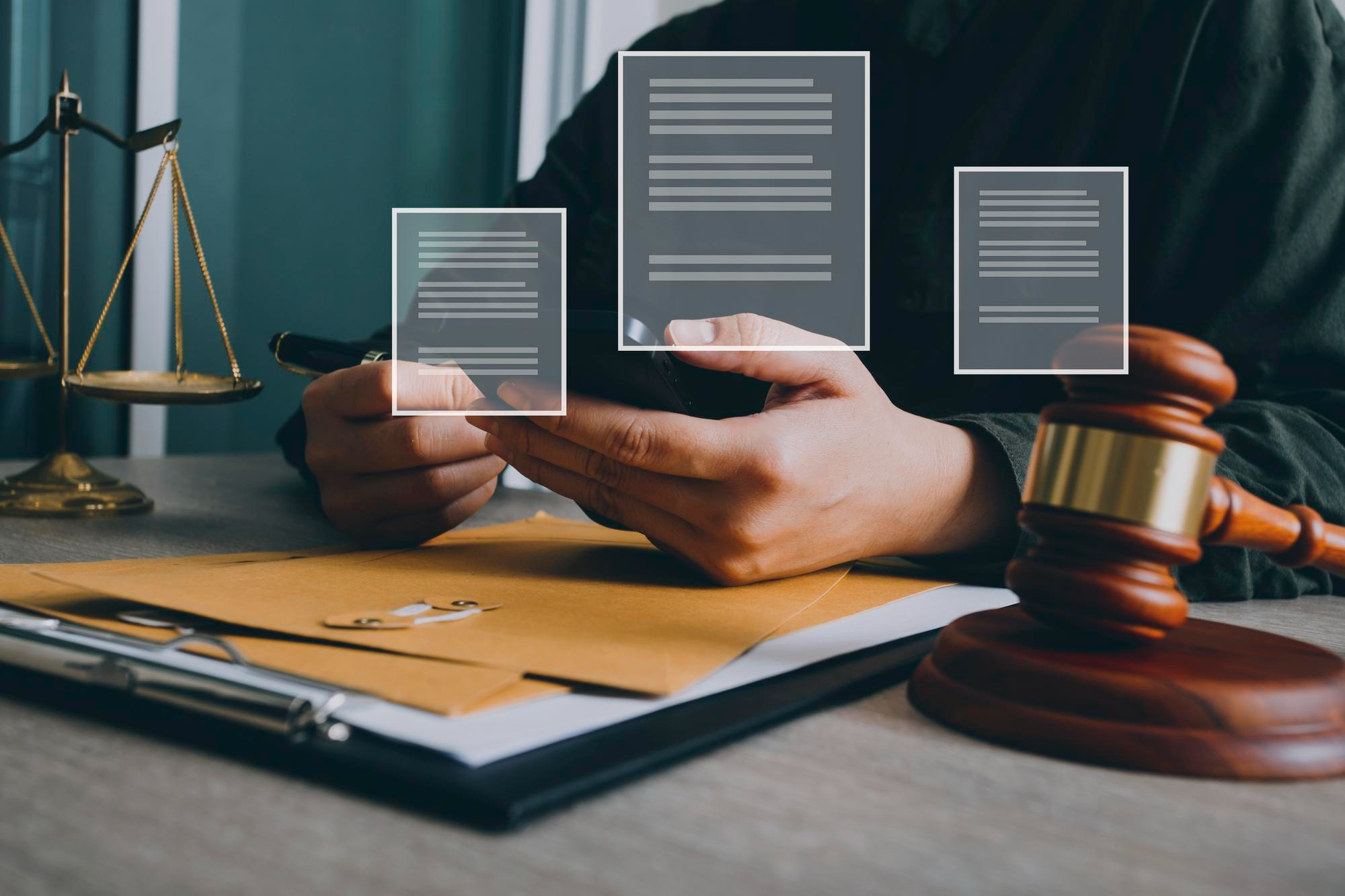 Lawyer or legal professional reviewing digital documents with virtual document icons floating above hands, with gavel, scales of justice, and legal files on desk