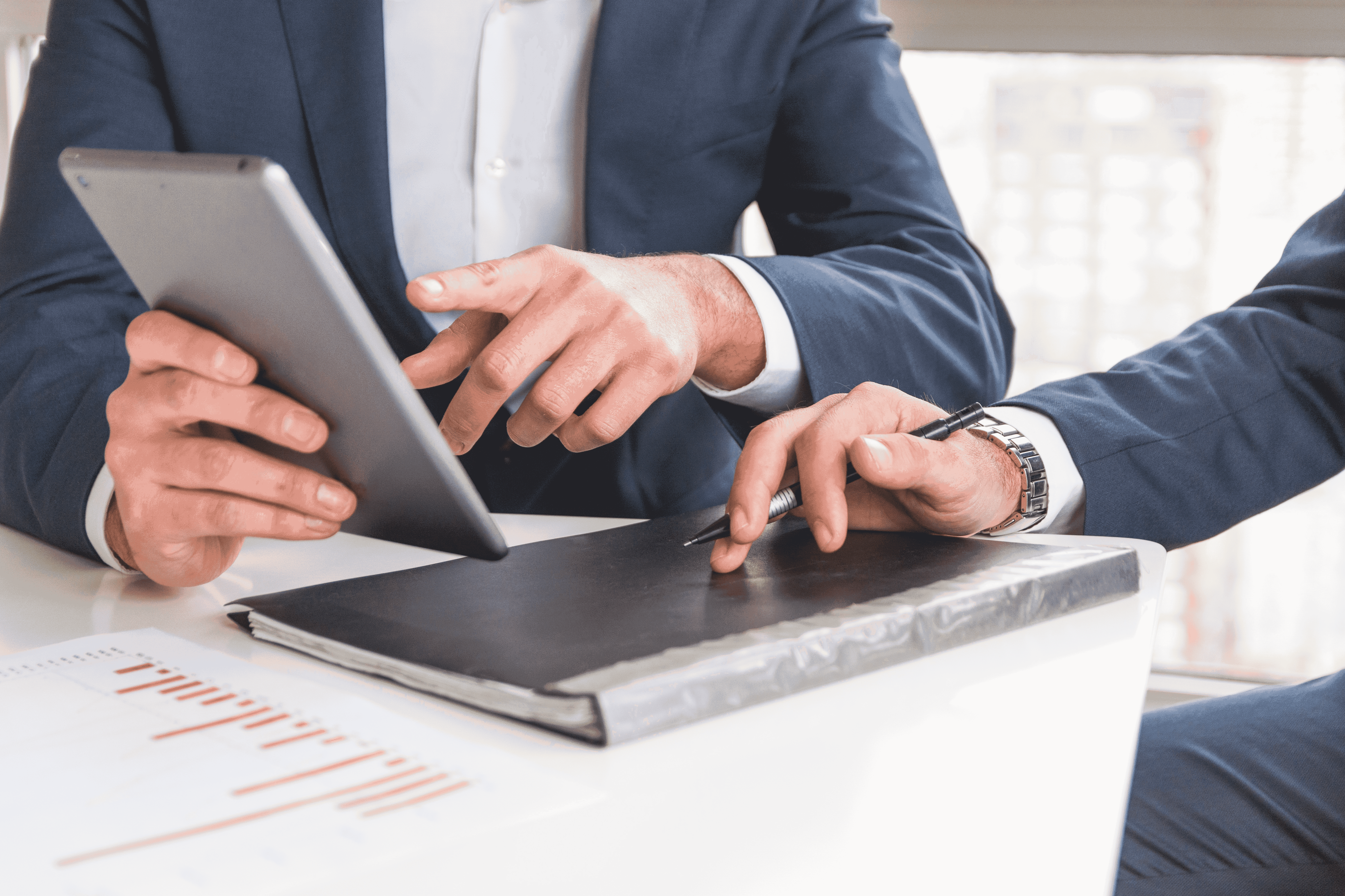 Business professionals in suits collaborating with tablet and digital pen over documents with charts at desk