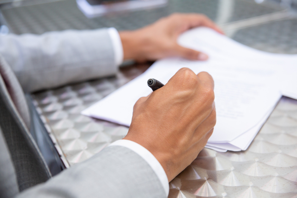 Close-up of a businessperson signing important documents by hand, representing the transition from traditional signatures to electronic signature apps for faster document processing.