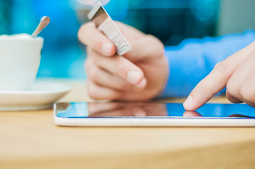Person using a tablet and holding a credit card to complete a digital transaction, symbolizing secure online signing and electronic document processing.